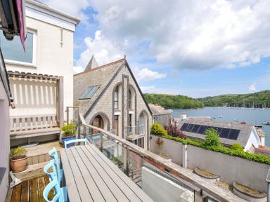 A balcony with wooden table and blue chairs overlooking a waterway with boats and green hills at 5 Esplanade in Fowey