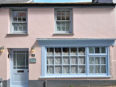 Exterior view of a house with light blue door and window frames and light pink walls at 5 Esplanade in Fowey