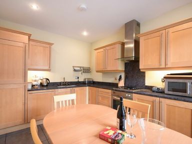A kitchen with wooden cabinets a round dining table with a bottle glass and a box on it at Churchside in Alnwick