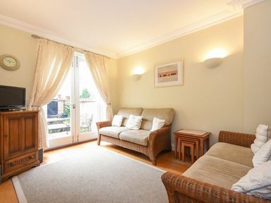 A sitting room with two sofas a wooden cabinet and glass doors with curtains at Churchside in Alnwick