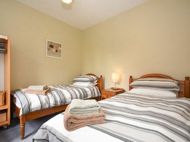 A bedroom with two single beds striped bedding a wooden side table with a lamp and a wooden shelving unit at Churchside in Alnwick
