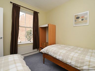 A bedroom with two single beds a wooden wardrobe with baskets and a window with brown curtains at Churchside Alnwick