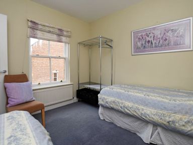 A bedroom with two beds a chair with a purple cushion a metal shelving unit and a window at Churchside in Alnwick