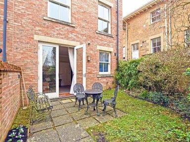 A small patio with metal table and chairs outside a brick house at Churchside in Alnwick