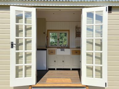 A kitchen with a farmhouse sink visible through open double glass doors at Shepherd Hut 1 in Northchapel