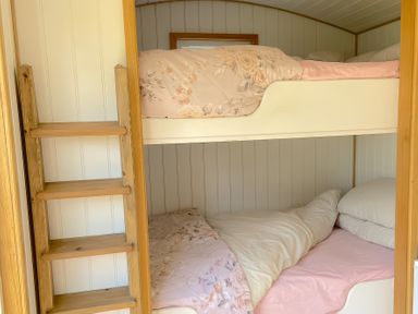 A wooden bunk bed with pink floral bedding and pillows at Shepherd Hut 1 in Northchapel