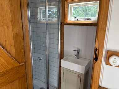 A bathroom with a glass door shower and a small sink under a window at Shepherd Hut 1 Northchapel