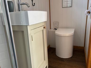 A small bathroom with a white sink on a beige cabinet and a modern white toilet at Shepherd Hut 1 in Northchapel