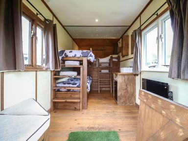 A small bedroom with bunk beds, wooden floor, windows with curtains, and a small desk at Buttercup (Cow Shed 3) in Easton near Campsea Ashe