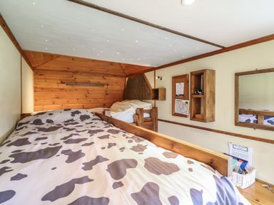 A small bedroom with two wooden beds one with cow print bedding and wooden shelves on the wall at Buttercup Cow Shed 3 in Easton near Campsea Ashe