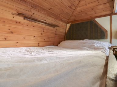 A bed with white bedding and wooden paneling on the walls in Buttercup Cow Shed 3 in Easton near Campsea Ashe