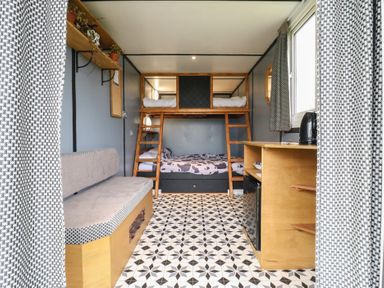 A room with bunk beds a bench a wooden cabinet with a kettle and a window with curtains at Dozy Dotty Cow Shed 4 in Easton near Campsea Ashe