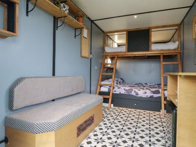 A room with a wooden bunk bed with cow print bedding a beige cushioned bench and patterned floor tiles at Dozy Dotty Cow Shed 4 Easton near Campsea Ashe