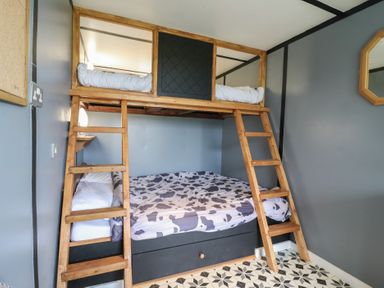 A bunk bed with wooden ladders and cow print bedding in a room with gray walls and patterned floor at Dozy Dotty Cow Shed 4 Easton near Campsea Ashe