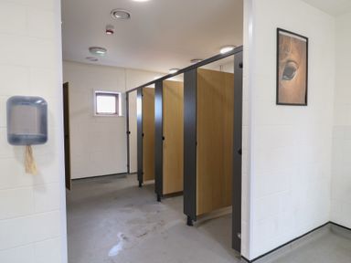 A restroom with multiple wooden stalls a paper towel dispenser and a framed picture on the wall at Dozy Dotty Cow Shed 4 Easton near Campsea Ashe