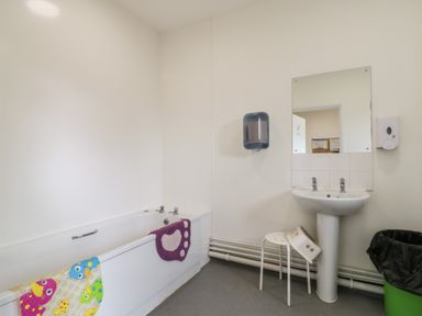 A bathroom with a bathtub a sink with two faucets a mirror and a green trash bin at Dozy Dotty Cow Shed 4 Easton near Campsea Ashe