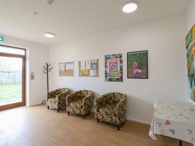A waiting area with three patterned armchairs a coat rack a table with a cloth and posters on the wall at Dozy Dotty Cow Shed 4 Easton near Campsea Ashe