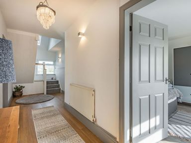 A hallway with wooden floor rugs a grey door and stairs leading up at Bryn Derw in Caernarfon