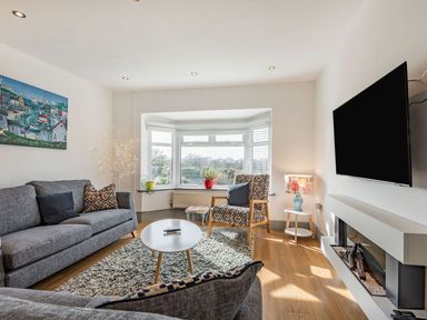 A living room with gray sofas a coffee table armchair bay window and a wall-mounted television at Bryn Derw in Caernarfon