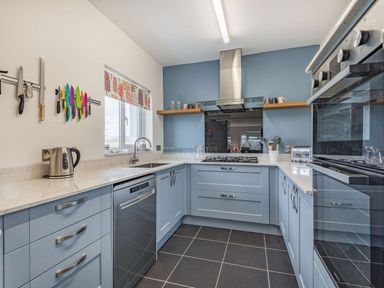 A kitchen with blue cabinets a gas stove a dishwasher and a knife rack on the wall at Bryn Derw in Caernarfon