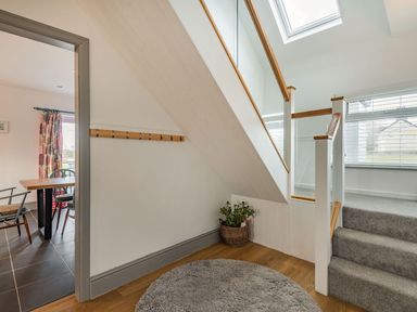 A stairway with grey carpet and wooden handrails next to a round rug and a basket with a plant at Bryn Derw in Caernarfon