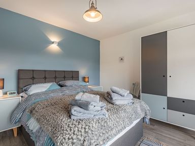 A bedroom with a double bed with folded towels bedside tables and a wardrobe at Bryn Derw in Caernarfon