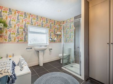 A bathroom with a bathtub a sink a toilet a glass shower enclosure floral wallpaper and a round rug at Bryn Derw in Caernarfon