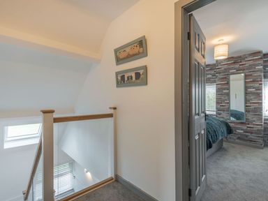 Upstairs hallway with framed pictures on wall and view into bedroom with textured wall at Bryn Derw in Caernarfon
