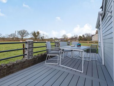 An outdoor deck with a table and four chairs overlooking a grassy field with sheep at Bryn Derw in Caernarfon