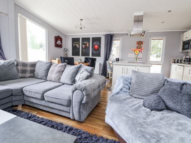 A living area with grey sofas pillows a kitchen island with flowers and a dining table with chairs at 155 Woodland Hall Lyons Ruthin