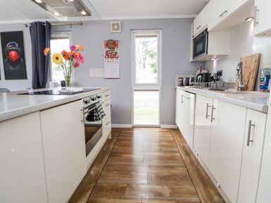 A kitchen with white cabinets and wooden floor with flowers on an island at 155 Woodland Hall Lyons in Ruthin