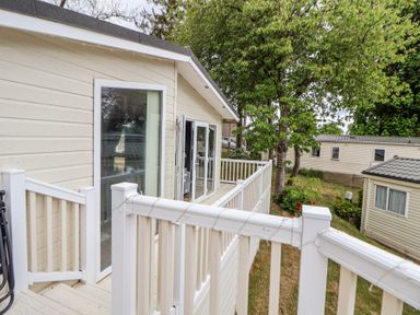 A balcony with white railing attached to a beige mobile home with trees and other mobile homes in the background at 155 Woodland Hall Lyons in Ruthin