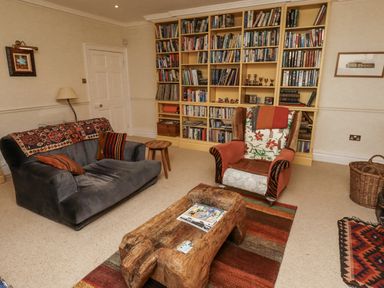 A living room with a bookshelf, sofa, and chair at Elford Farmhouse in Seahouses