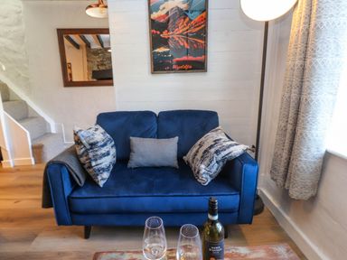 A blue sofa with cushions in a living room with a bottle of wine and glasses on a wooden floor at 4 Old Tanrhiw in Beddgelert