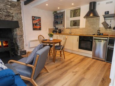 A kitchen and dining area with a round wooden table and chairs a stove and dishwasher and a wood burning stove at 4 Old Tanrhiw in Beddgelert