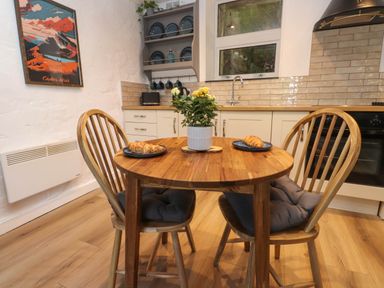 A kitchen with a wooden table and two chairs with cushions two plates with croissants and a plant centerpiece at 4 Old Tanrhiw in Beddgelert