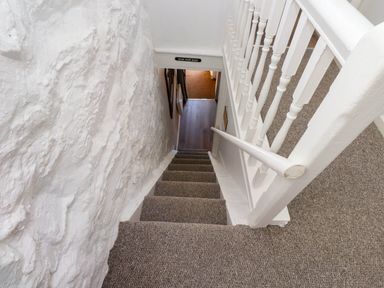 A narrow staircase with carpet leading down between a white textured wall and a white wooden railing at 4 Old Tanrhiw in Beddgelert