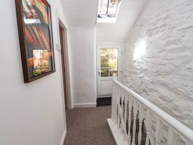 A hallway with a carpeted floor a white wooden banister a door with glass panes and a framed picture on the wall at 4 Old Tanrhiw in Beddgelert