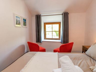 A bedroom with a bed a window with curtains two red chairs and framed pictures on the wall at 4 Old Tanrhiw in Beddgelert