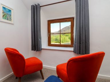 A small room with two orange chairs facing a window with gray curtains and a painting on the wall at 4 Old Tanrhiw in Beddgelert