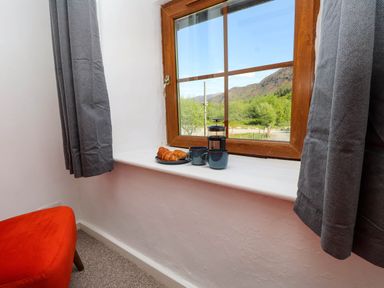 A window with gray curtains showing a view of trees and mountains with croissants and mugs on the windowsill at 4 Old Tanrhiw in Beddgelert