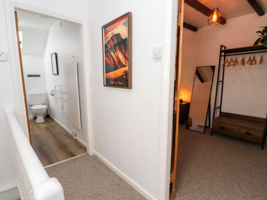 Hallway with a framed picture on the wall leading to a bathroom with a toilet and a room with a clothing rack and a full-length mirror at 4 Old Tanrhiw in Beddgelert