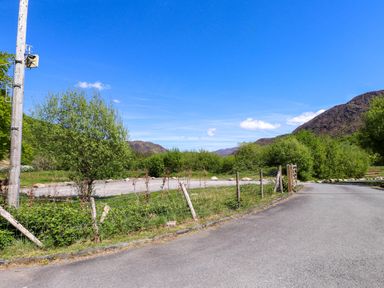 A road next to a wire fence with trees and hills in the background at 4 Old Tanrhiw in Beddgelert