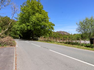 A two lane road lined with trees and bushes under a clear blue sky at 4 Old Tanrhiw in Beddgelert