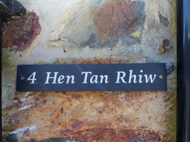 A house sign with the text 4 Hen Tan Rhiw on a stone wall at 4 Old Tanrhiw in Beddgelert