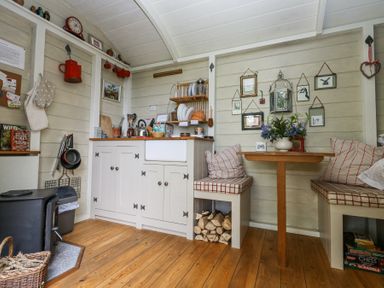 A small kitchen and dining area with wooden floor cabinets dishes and a wood stove at Sika in Warmwell