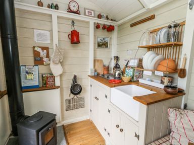 A small kitchen with a wood stove and sink with dishes on a rack at Sika in Warmwell
