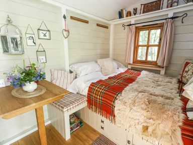 A small room with a bed covered with a red plaid blanket and sheepskin next to a wooden table with flowers at Sika in Warmwell