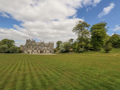 A large grassy field with a stone building and trees under a partly cloudy sky at Sika in Warmwell