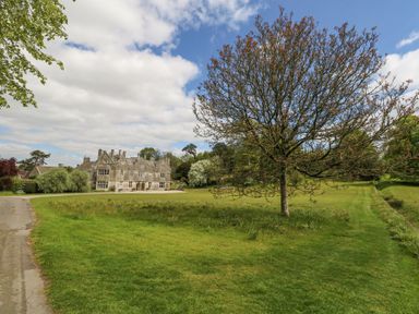 A large stone house with multiple chimneys surrounded by grass and trees at Sika in Warmwell